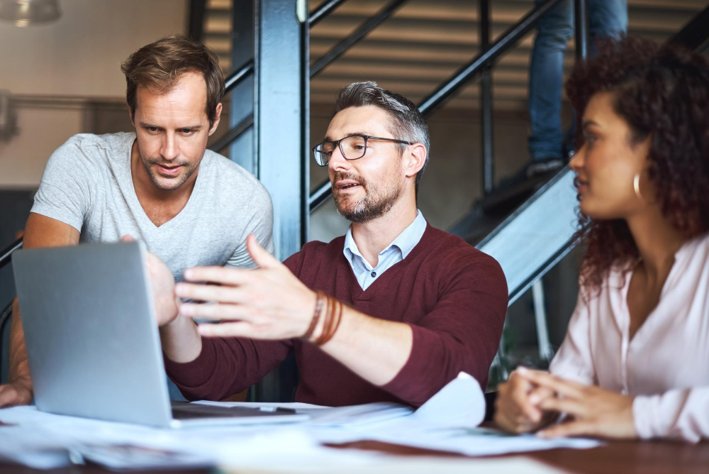 Three professionals collaborating around a laptop in a modern office